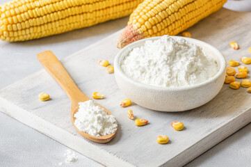 Corn starch in bowl and spoon with dried corn groats, kernels on rustic table. Maize starch with ripe cobs and kernels