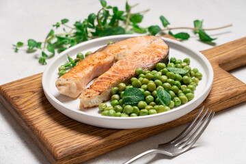 Roasted salmon steak with fresh green peas and mint on white plate. Healthy food light background with copy space