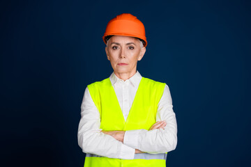 Confident mature woman in safety gear standing against dark blue background, representing professionalism