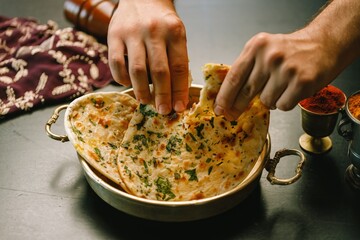 A skilled hand delicately pulls apart warm naan bread from a traditional steel bowl, surrounded by colorful spice containers, bringing the essence of Indian cuisine to life
