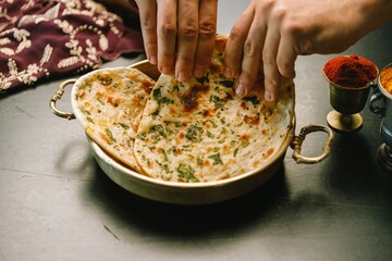 Delicate hands gently place aromatic Indian flatbreads on a traditional brass plate. The vibrant spices and herbs contrast beautifully on the dough, creating a rich culinary experience