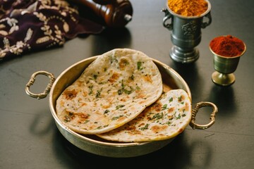 Freshly baked flatbreads are artfully arranged on a brass platter, accompanied by bowls of aromatic spices. The rich colors and textures showcase the essence of traditional Indian cuisine