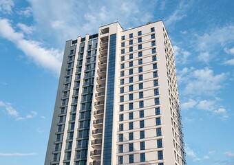 Obraz premium Modern high-rise condominium with sleek facades and windows, contemporary urban architecture in a vibrant city district, luxury residential real estate under a sunny sky.