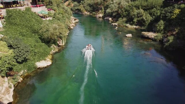 Tourist activity of boat ride in the Neretva river passing under the Stari Most, Mostar old bridge. Aerial video of the speedboat going fast in the river in the middle of the town.