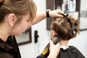 Child receiving a haircut in a modern salon during daytime with a focused stylist