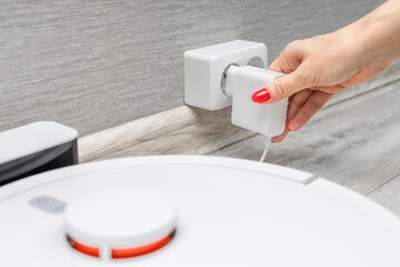 a woman's hand connects a robot vacuum cleaner charger to the power supply. charging station for...