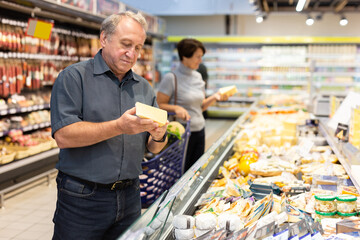 Elderly man choose cheese in supermarket