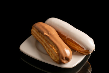 Two eclairs with cream filling on a ceramic saucer, close-up, isolated on a black background.
