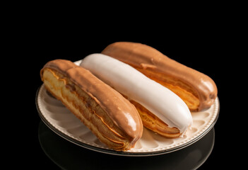 Three eclairs with cream filling on a ceramic saucer, close-up, isolated on a black background.