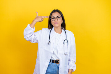 Young brunette doctor woman wearing stethoscope standing over isolated yellow background Shooting and killing oneself pointing hand and fingers to head like gun, suicide gesture.