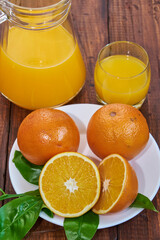 Freshly squeezed orange juice, refreshing and healthy, on a rustic wooden table with whole oranges and green leaves.