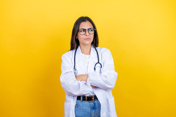 Young brunette doctor woman wearing stethoscope standing over isolated yellow background thinking looking tired and bored with crossed arms