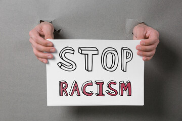 Man holding paper with text Stop Racism through holes in grey paper, closeup