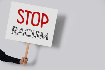 Woman holding sign with text Stop Racism on light grey background, closeup. Space for text