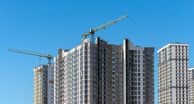 Modern residential building under construction with a crane, high-rise structure featuring contemporary facades and balconies, urban real estate development in a growing district.