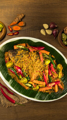 Indonesian traditional gurame pesmol, A beautifully presented fish dish, adorned with vibrant spices and fresh vegetables, sits on a banana leaf ready for serving