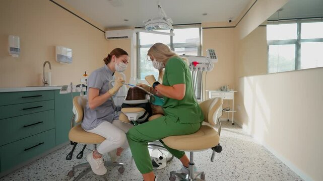Blonde Woman Dentist with Assistant Treat Teeth of Female Patient with Special Instrument. Treatment of Caries and Plaque in Dental Clinic. Concept of Medicine and Healthcare. Slow Motion.