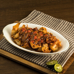 Indonesian traditional batagor, Fried snacks are beautifully arranged on a plate, garnished with sauce and accompanied by fresh lime wedges on a striped cloth