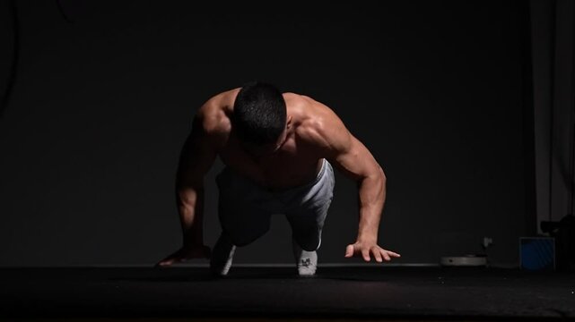 Muscular man demonstrates extreme strength performing push-ups in a dark gym setting. Concept fitness, power, endurance, discipline, focus, body control, and dedication.