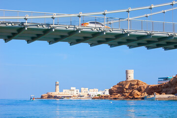Oman, Sur, a car crosses the suspension bridge on the coast; the small lighthouse and the...