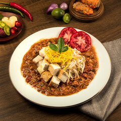 Indonesian traditional ketoprak, A colorful vegetarian dish showcases tofu, noodles, and fresh vegetables arranged attractively on a wooden table with spices nearby