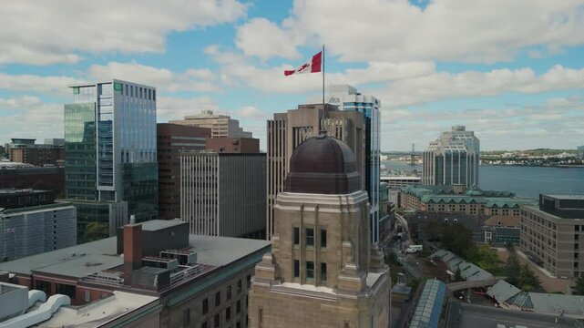 Aerial View Of An Ancient Skyscraper With A Waving Flag On The Tower At Sunset In Halifax. Modern Skyscrapers Frame The Scene, Highlighting The Contrast Between Old And New Architecture.