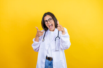 Young brunette doctor woman wearing stethoscope standing over isolated yellow background pointing to you and the camera with fingers, smiling positive and cheerful