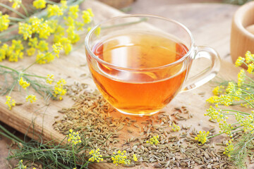 Fennel seed tea or extract on wooden background with fresh flowers nearby, copy space, natural medicine, drink for breast milk production, sleep and stress care tea concept