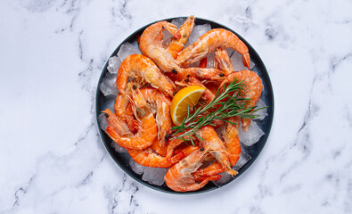 Freshly frozen shrimp on ice, with lemon and rosemary, on the marble table, top view, no people