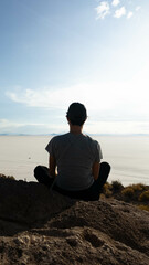 silhouette of a unrecognizable traveler meditating on a rock on the island of Incahuasi in the Uyuni salt flat in Bolivia