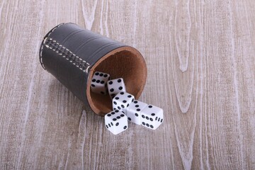 leather dice cup lies on the wooden table and white dice fall out