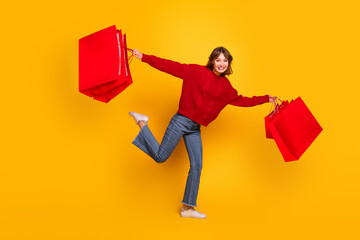 Cheerful young woman holding red shopping bags in a colorful setting, expressing joy and excitement...