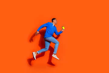 Fototapeta na wymiar Energetic young man in vibrant blue shirt against striking orange background jumping