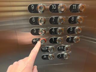 A hand presses the silver button inside an elevator © JackCA