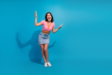 Energetic young woman posing in casual summer outfit against bright blue background, expressing joy...