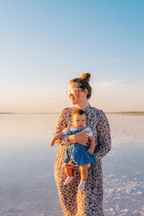 A loving mother lifting her happy baby during a warm sunset by a scenic lake, radiating joy and serenity.