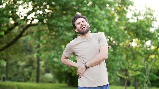 Sportsman suffering from back pain, sports injury, muscle spasm during a morning run in the urban city park. Young adult runner having back flank ache and problem after exercise outside in nature