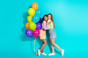 Fototapeta premium Two happy young women embracing amidst vibrant balloons, sharing a joyful and stylish moment against a vibrant turquoise background
