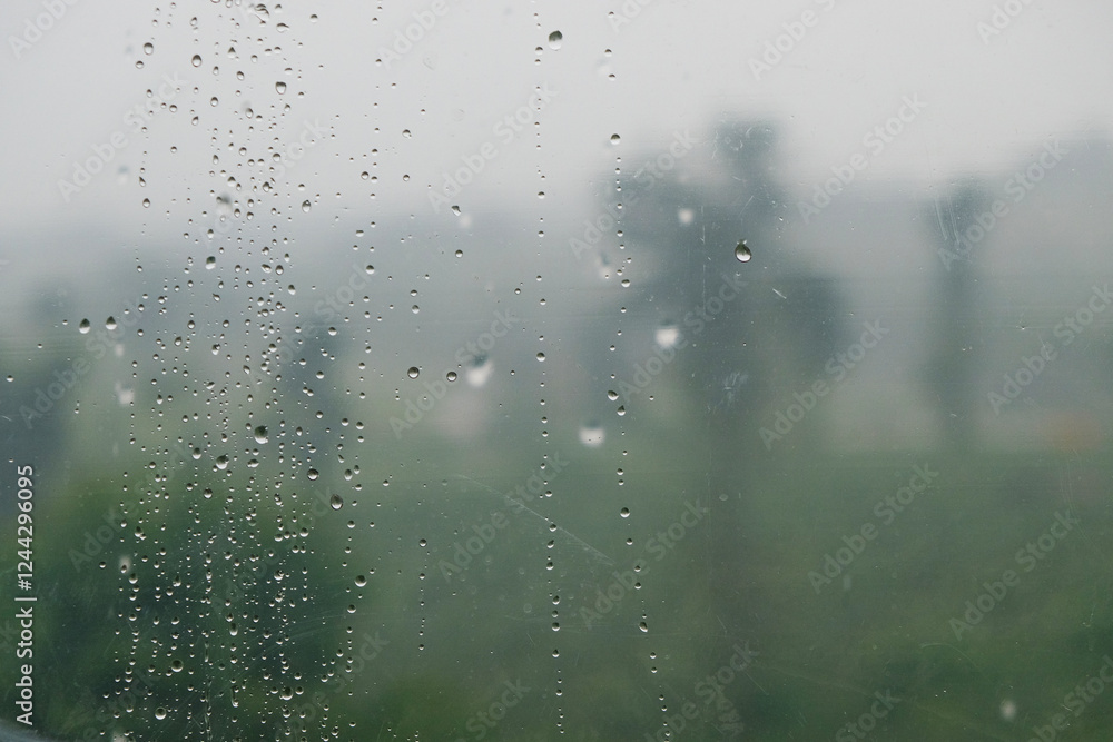Poster abstract pattern and texture of raindrops on transparent plastic with a blurry landscape background.