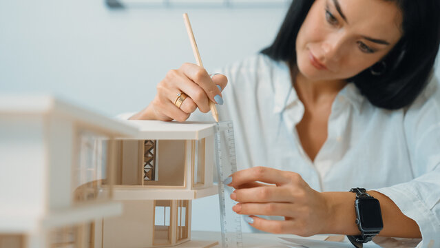 Closeup portrait image of professional young beautiful engineer architect using triangular scale measures house model with focusing at modern office. Business creative design concept. Immaculate.