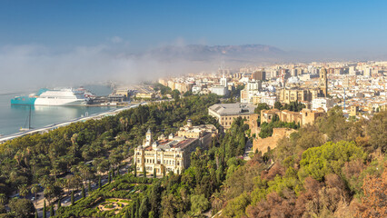 Malaga, seaside city in Andalusia, Spain, Europe. Coastal city panorama with harbor, cruise ship, and historic buildings nestled amongst lush greenery under a clear sky.
