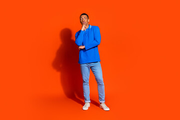 Young man in blue shirt posing thoughtfully against bright orange background