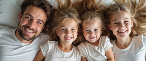 Obraz premium A cheerful family of four lies together on a soft, white bed, their hair cascading around them like golden waves. The radiant smiles of the father and his three daughters create a heartwarming scene