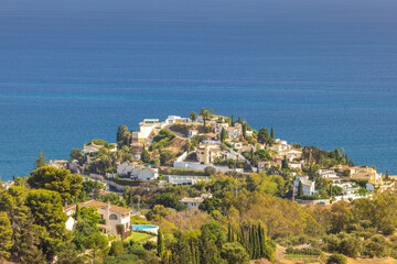 Obraz premium Coastal hillside homes overlooking the ocean. Luxury villas nestled amongst lush greenery and a stunning blue sea.