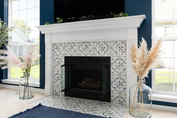 A fireplace detail with a white mantel surrounding white pattern tile on blue walls with bright windows surrounding.