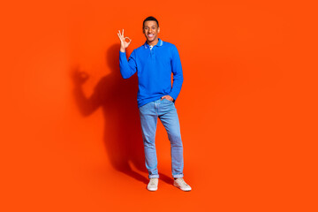Fototapeta premium Young man in blue shirt gesturing okay against vibrant orange background