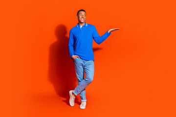 Young man in blue polo shirt posing against a vibrant orange background