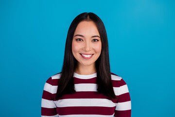 Fototapeta premium Portrait of a young woman in a striped shirt smiling against a blue background, showcasing a cheerful and modern vibe
