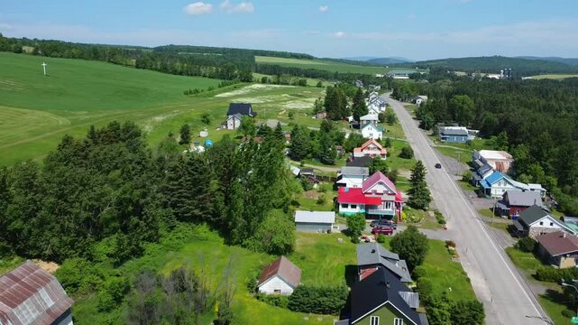 Aerial drone video of a car driving through the rural village of Saint‑Zenon‑du‑Lac‑Humqui along a scenic resort lake in the Matapedia Valley, Quebec, Canada