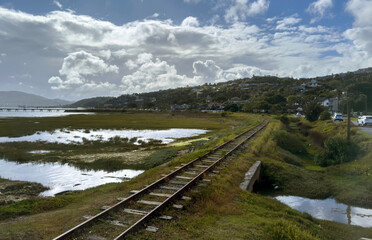 Fototapeta premium Abandoned railway track on a coatal wetland landscape, dramatic clouds sky, South Africa